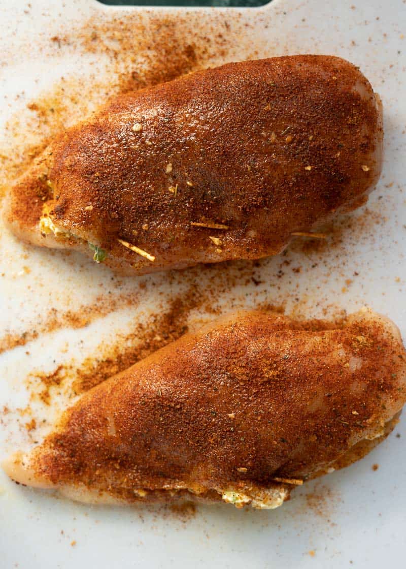 raw chicken breasts stuffed with cheesy jalapeno mixture, secured shut with toothpicks, and seasoned