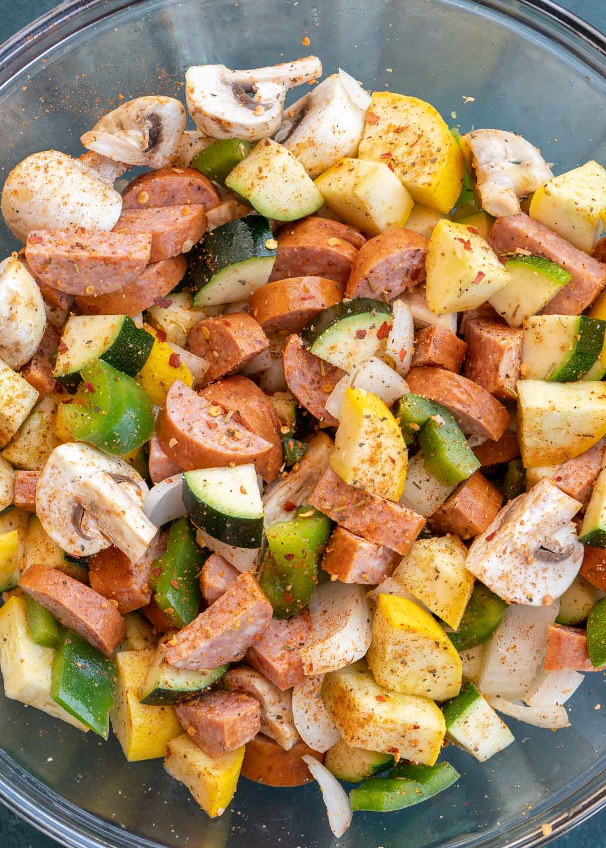 Seasoned sausage and veggies in clear mixing bowl