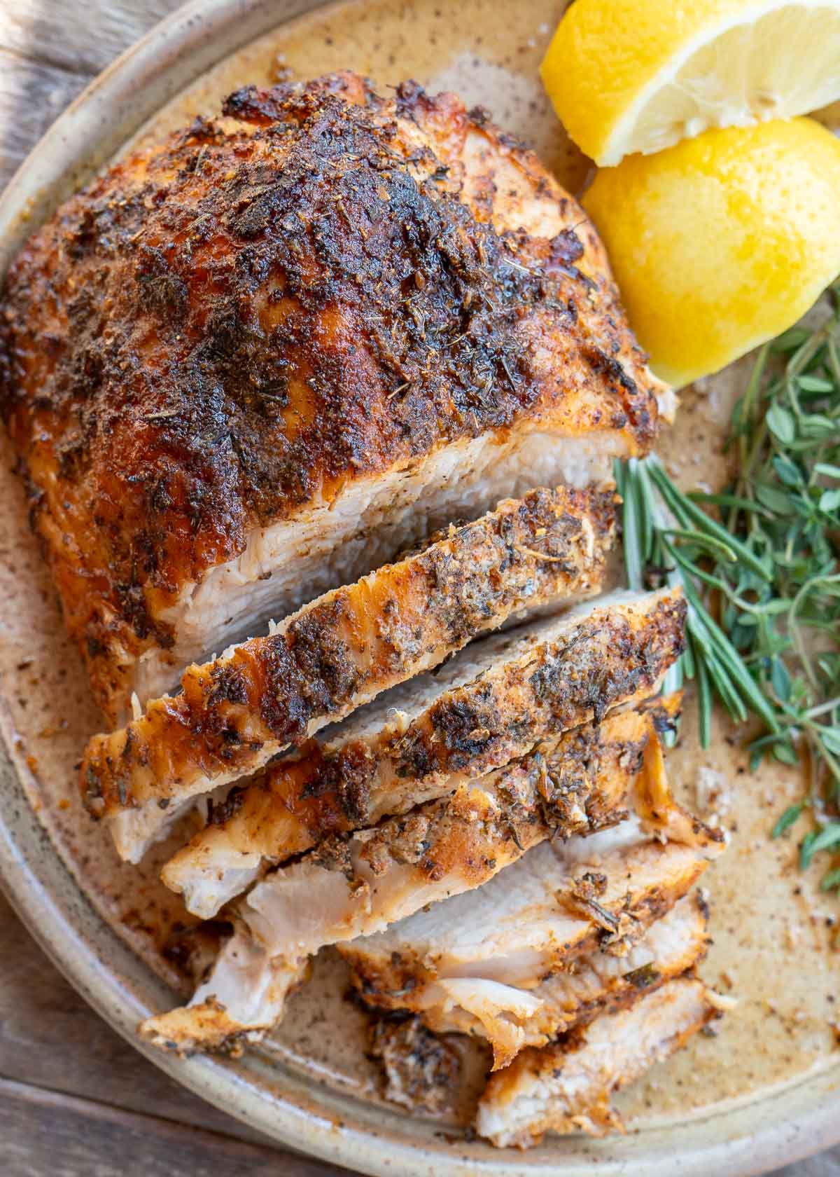 a sliced turkey breast on a plate with fresh herbs and lemon