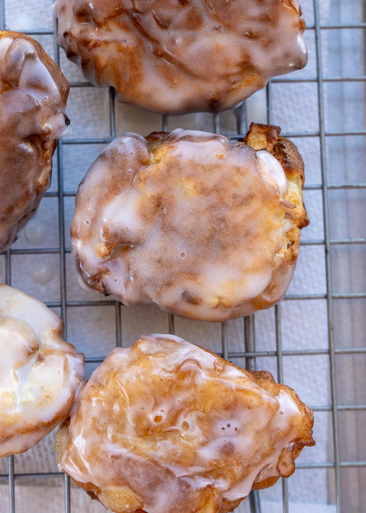 glazed apple fritters on a baking rack with paper towels underneath