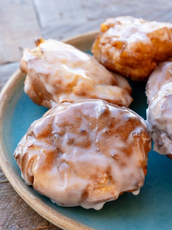 four glazed air fryer apple fritters on a teal plate