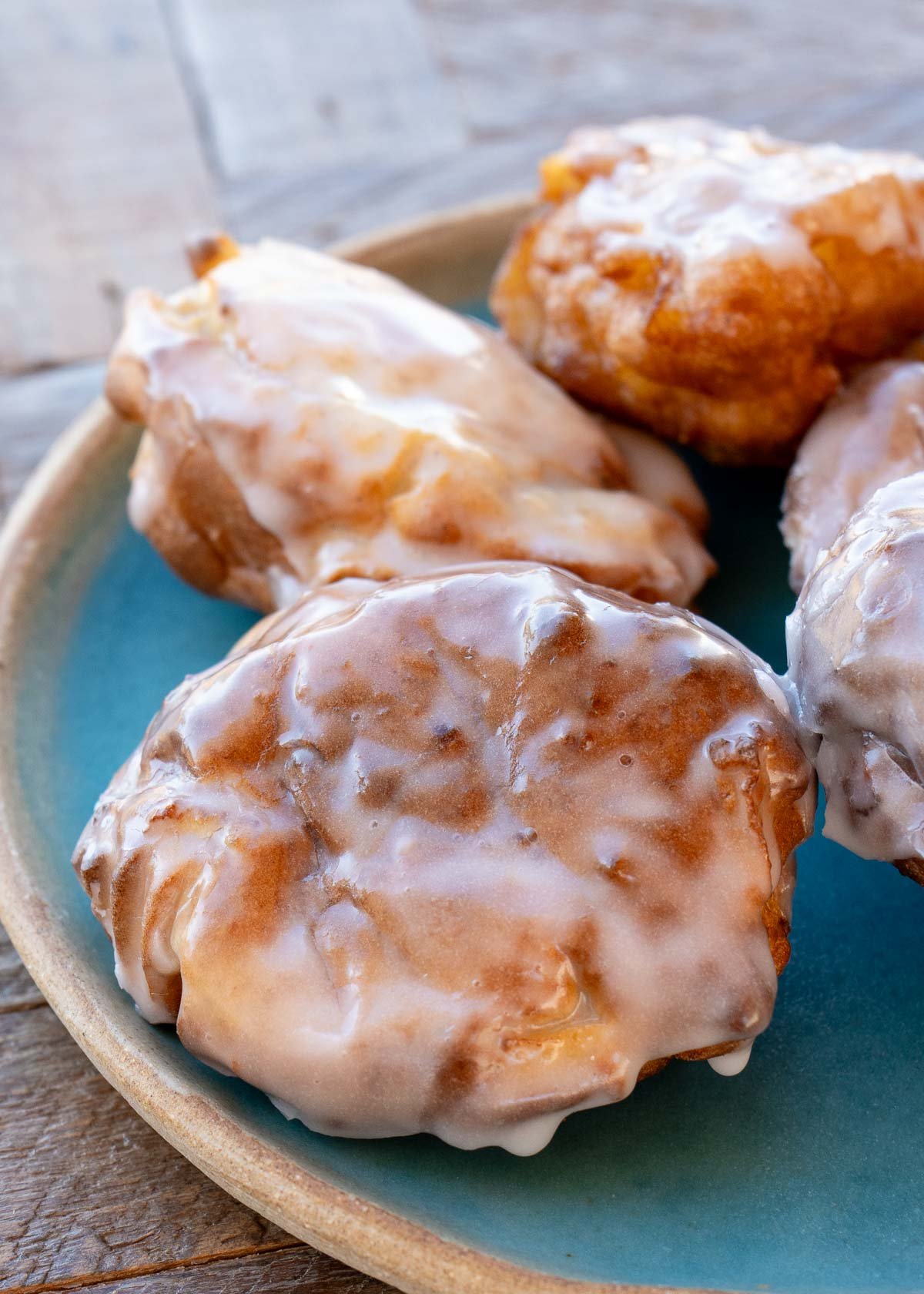 four glazed air fryer apple fritters on a teal plate