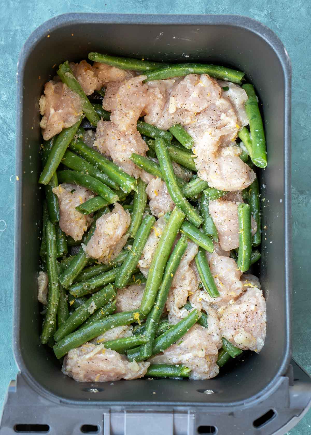 uncooked, seasoned chicken and green beans in the air fryer