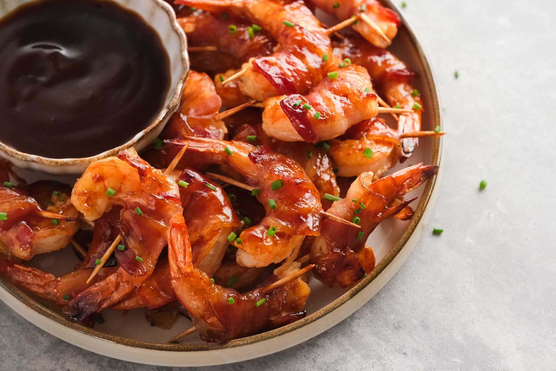 bacon wrapped shrimp on a plate with a small bowl of bbq sauce for dipping