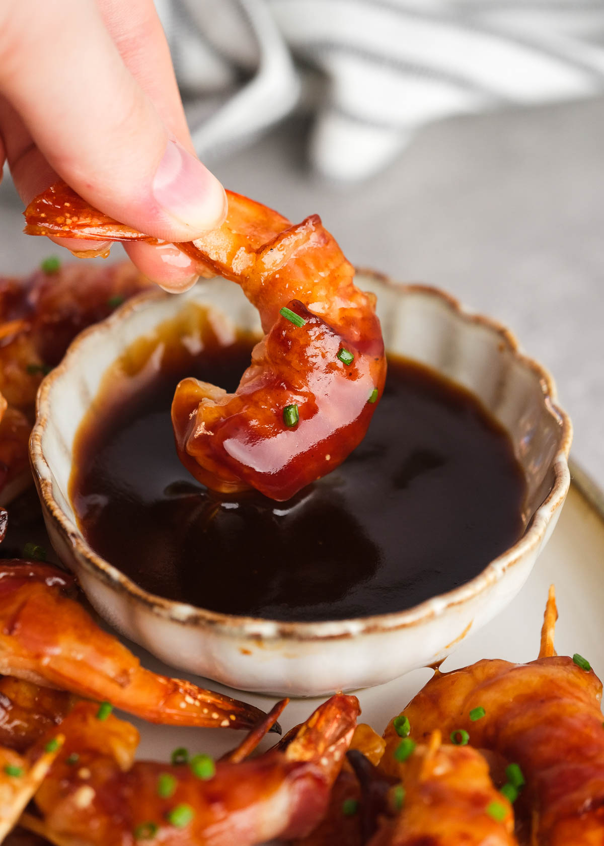 hand holding a bacon-wrapped shrimp in a bowl of bbq sauce