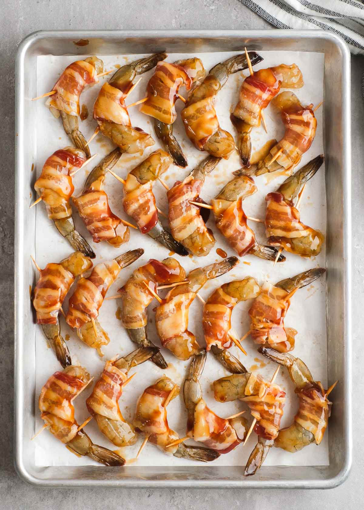 bacon wrapped shrimp covered in bbq sauce on a lined baking sheet
