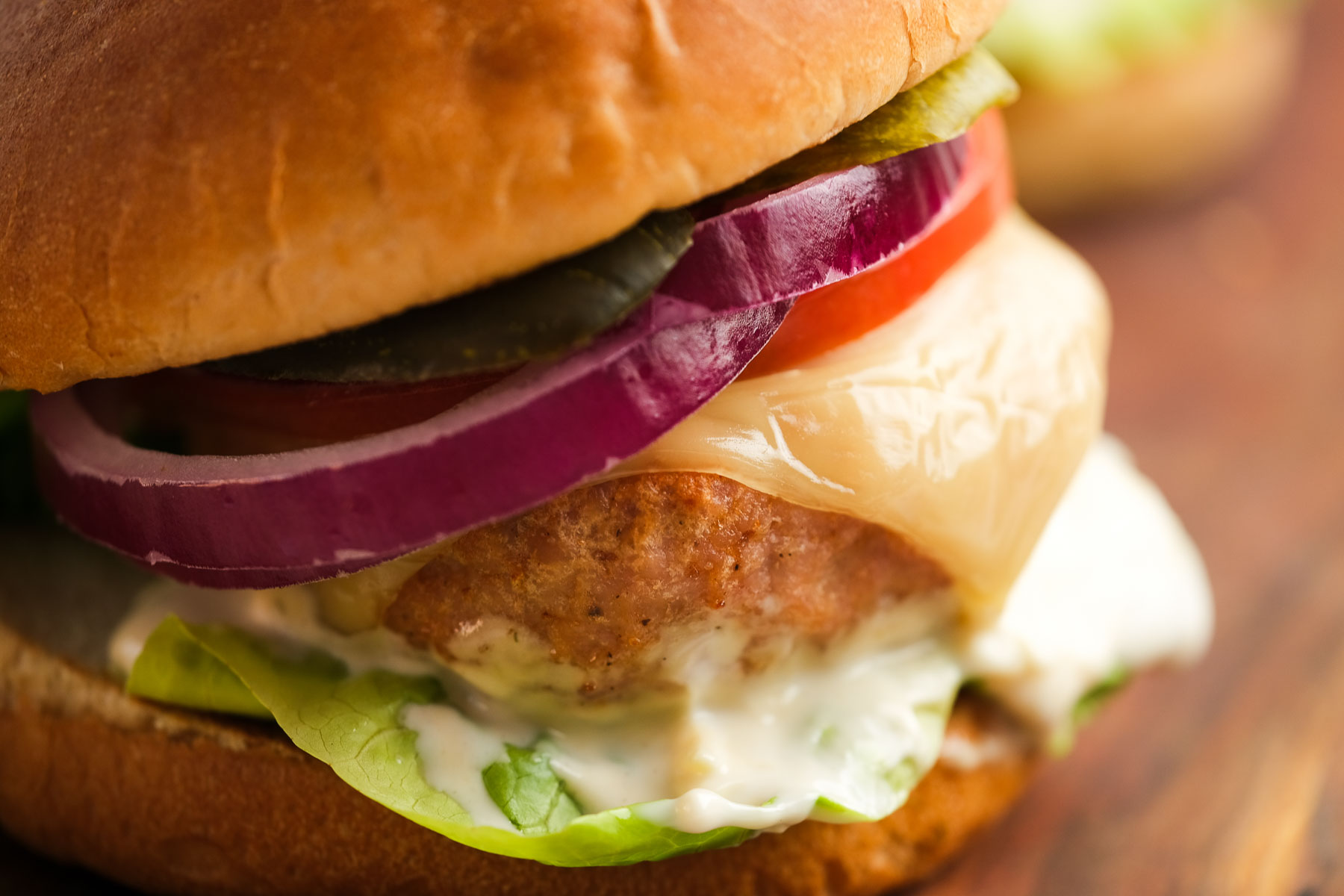 closeup image of a turkey burger with cheese, tomato, red onion, pickles, lettuce, and mayonnaise