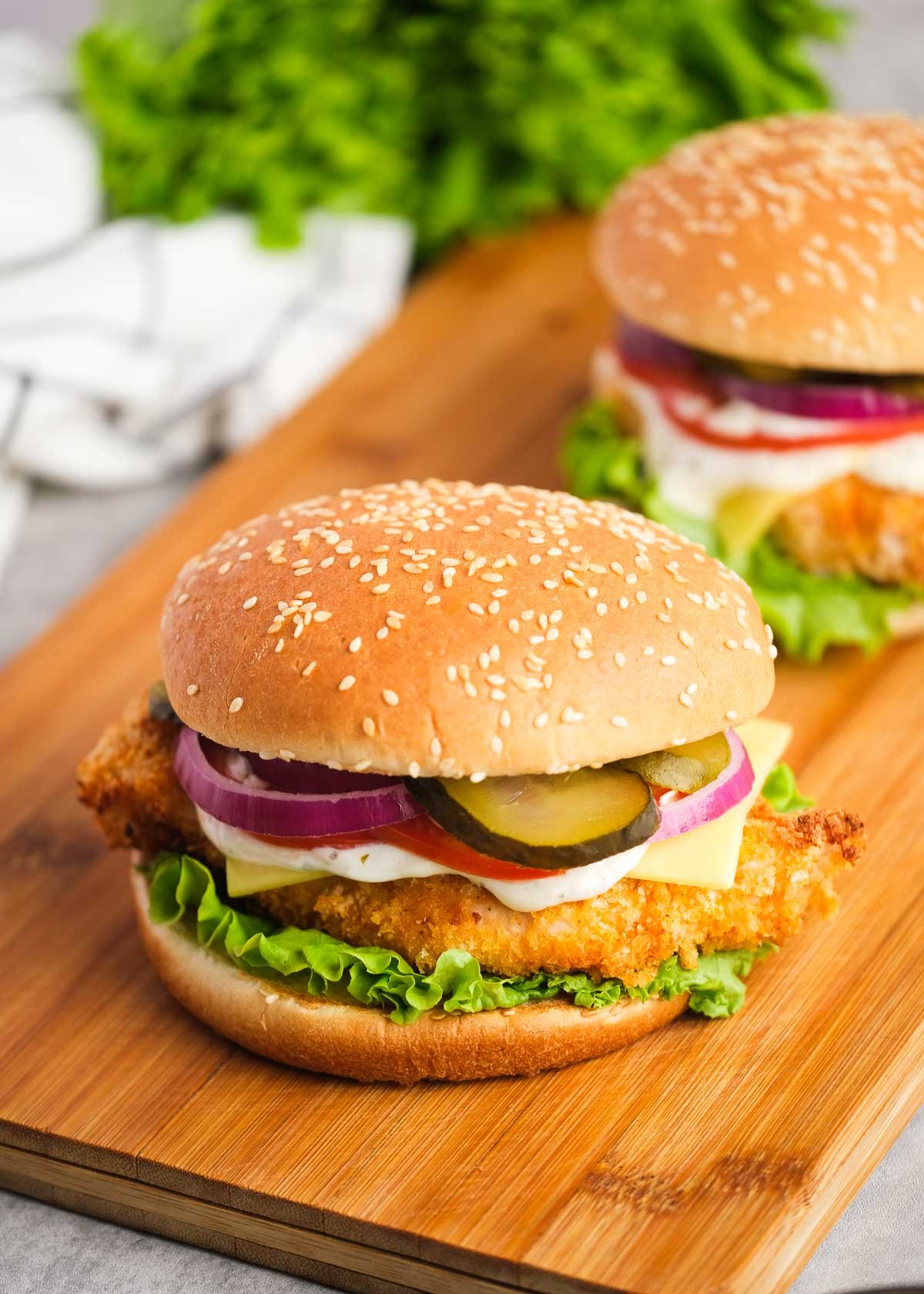 two crispy chicken sandwiches with tomatoes, cheese, mayo, pickles, red onions, and lettuce with a sesame bun