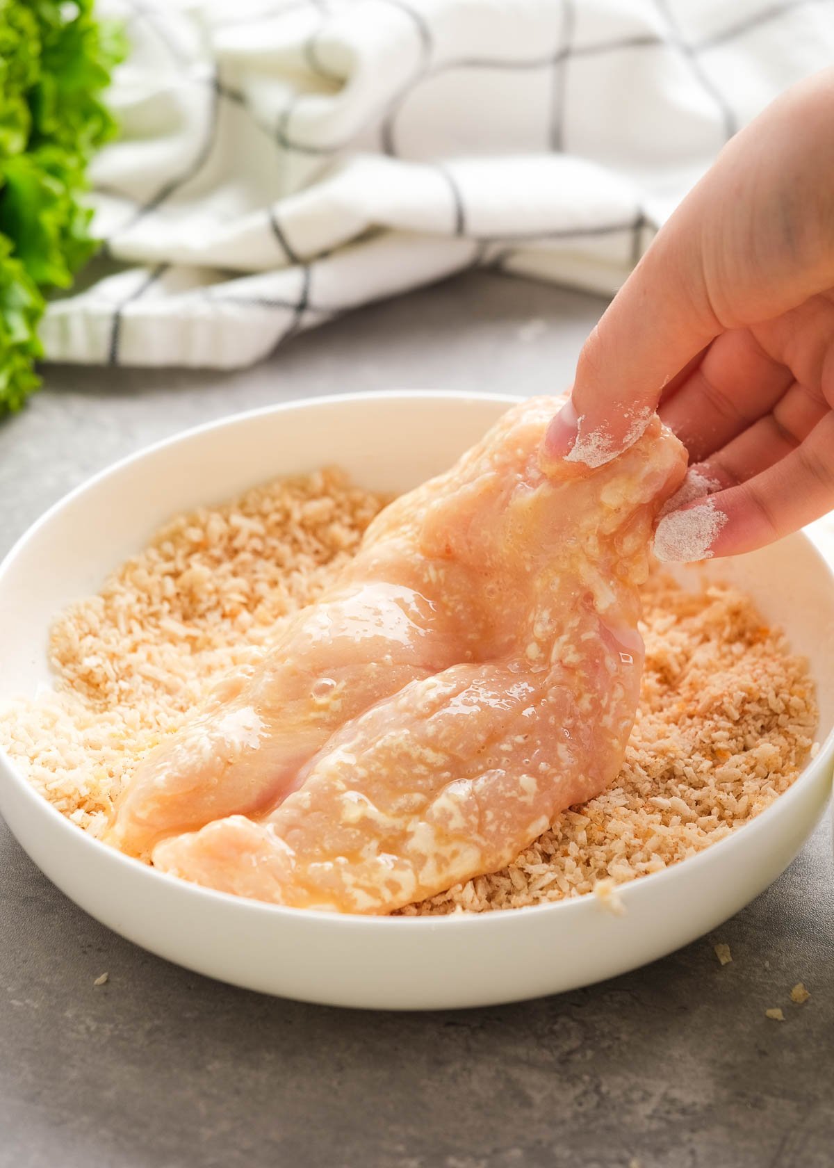 an egg-drenched chicken fillet being pressed into seasoned bread crumbs and parmesan cheese