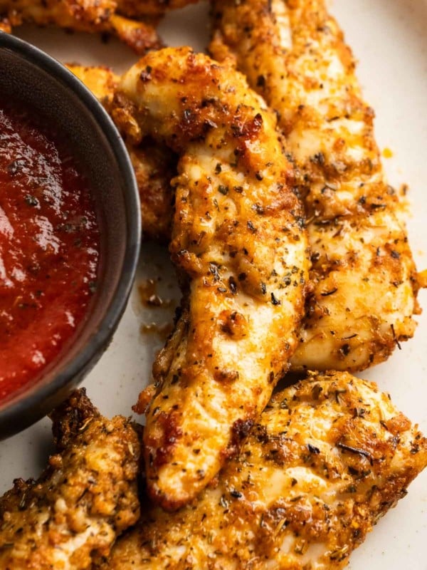a closeup shot of parmesan crusted chicken tenders on a plate with dipping sauce