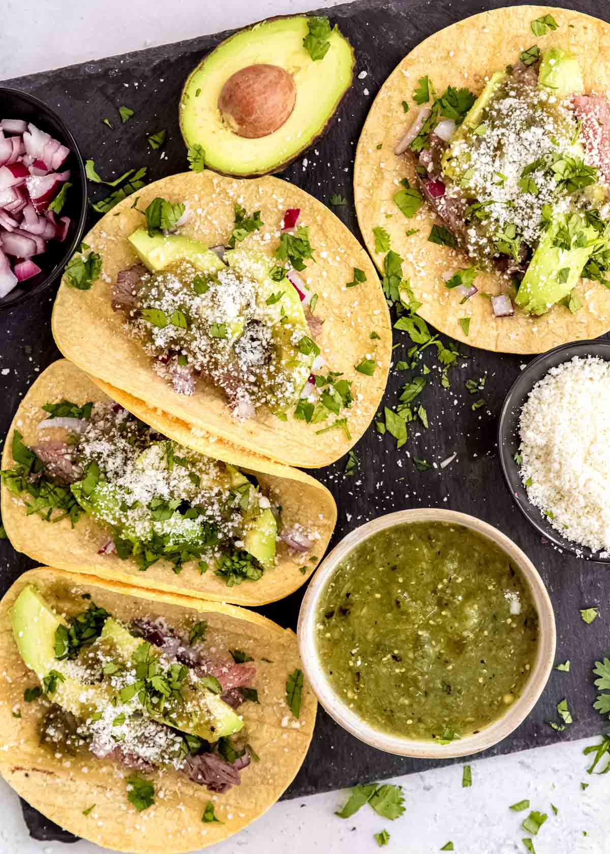 steak tacos with toppings on a board with salsa verde