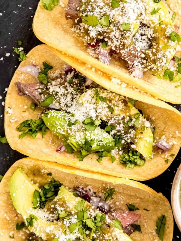 An overhead shot of steak tacos with avocado and salsa verde