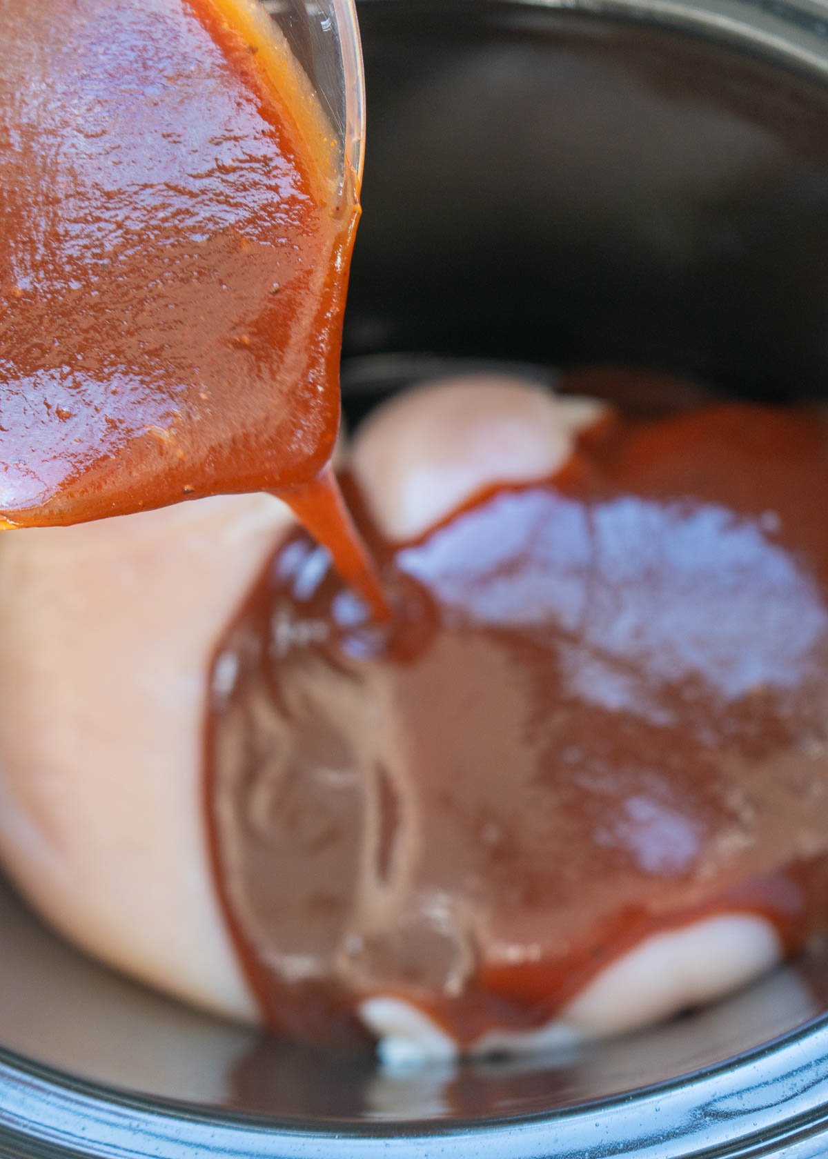 bbq sauce mixture being poured over chicken breasts in the slow cooker