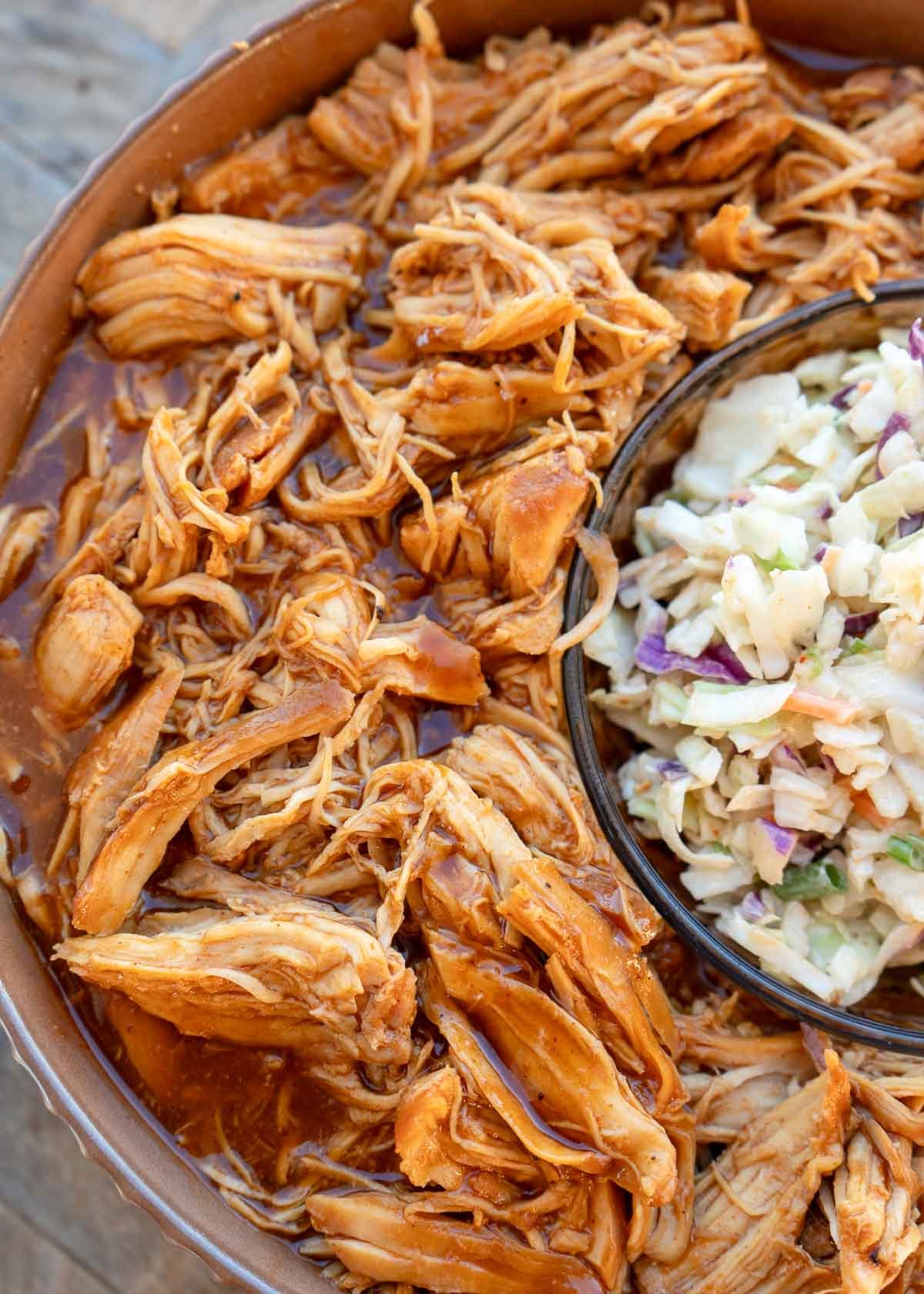 a bowl of coleslaw surrounded by juicy bbq chicken from the crock pot