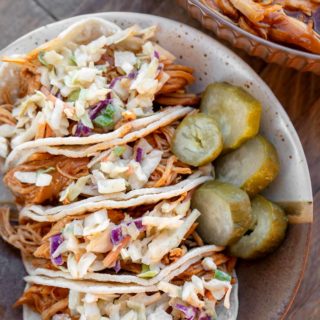 four bbq chicken tacos covered with easy coleslaw on a plate with pickles