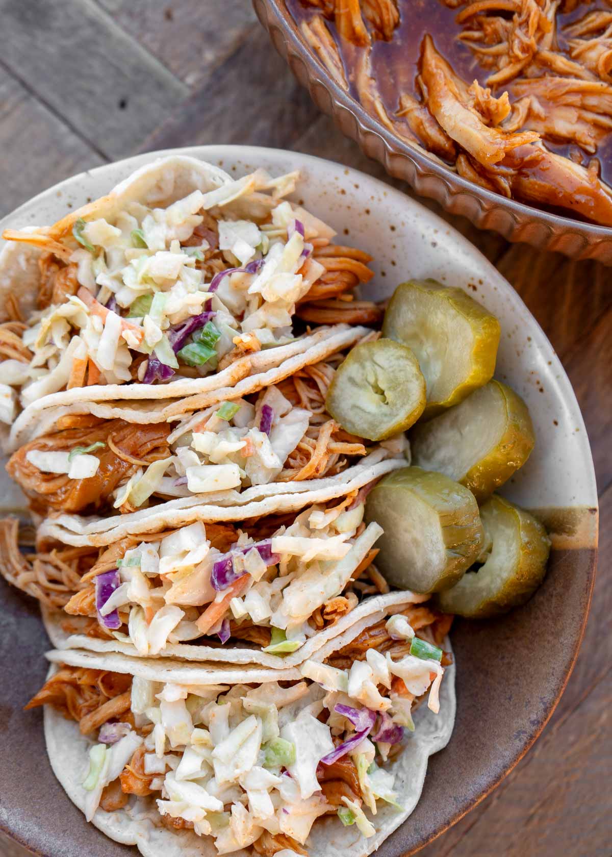 four bbq chicken tacos covered with easy coleslaw on a plate with pickles
