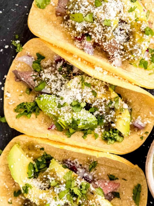 An overhead shot of steak tacos with avocado and salsa verde