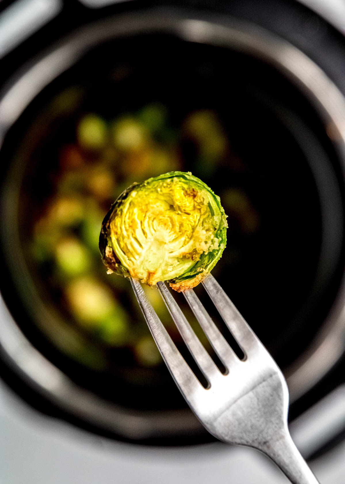 a fork holding a perfectly air fried brussels sprout over an air fryer full of them