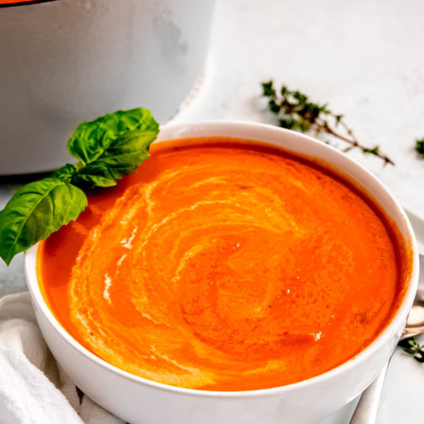the best roasted red pepper soup in a white bowl with fresh basil and thyme