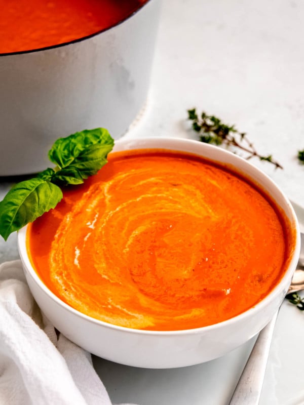 the best roasted red pepper soup in a white bowl with fresh basil and thyme