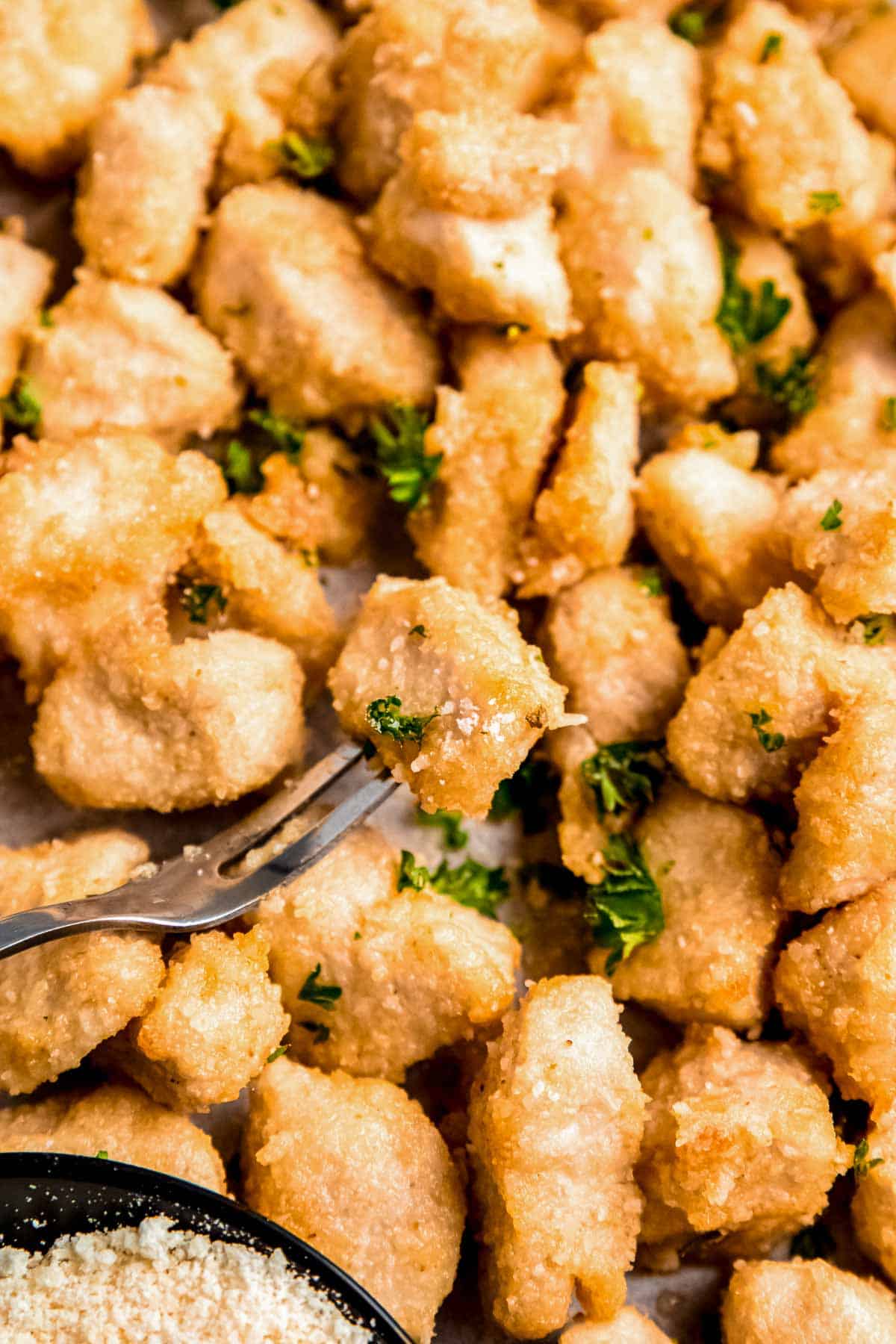 one chicken bite on fork in foreground with chicken bites on baking sheet below