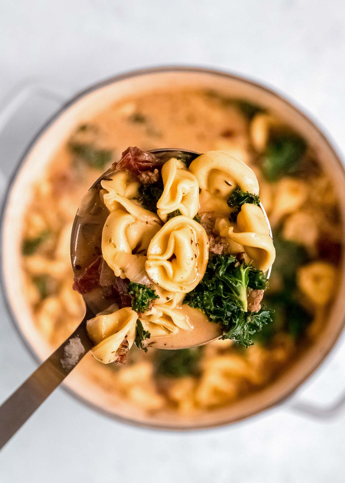 a spoon full of creamy soup, tender sausage, and delicious tortellini