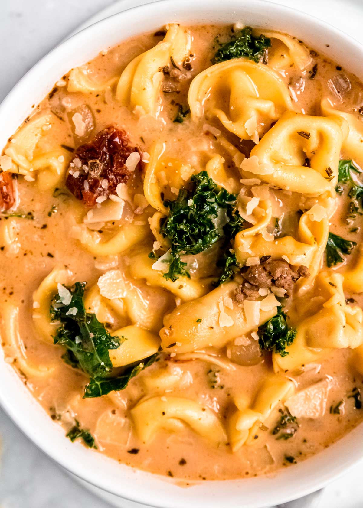 closeup shot of creamy soup with italian sausage, cheese tortellini, kale, and sundried tomatoes