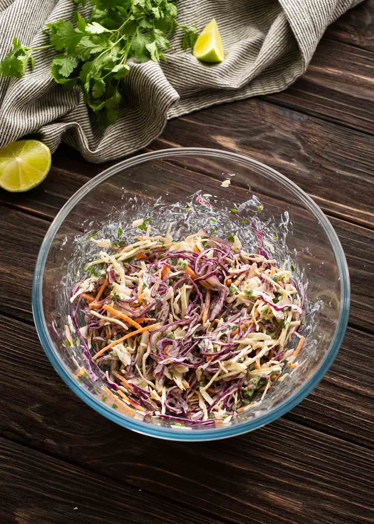 slaw ingredients being mixed in a clear mixing bowl