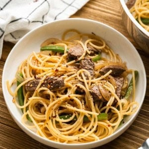 A bowl of sesame noodles with steak topped with sesame seeds