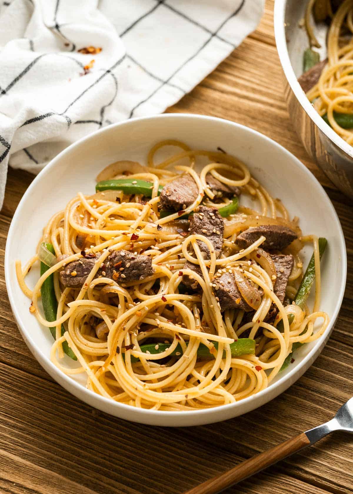 A bowl of sesame noodles with steak topped with sesame seeds