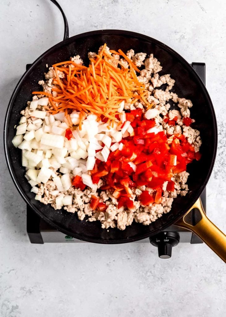 red bell pepper, carrots, onion, and garlic in a skillet with browned chicken and sesame oil