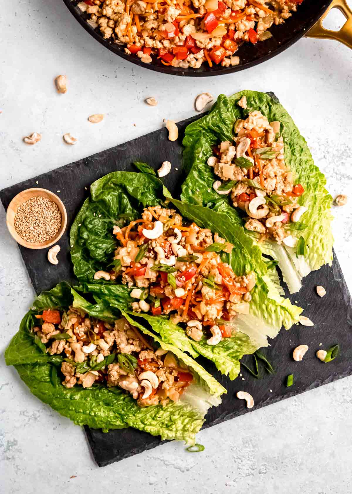 overhead zoomed out shot of thai chicken lettuce wraps garnished with peanut sauce, green onions, crushed cashews, and sesame seeds