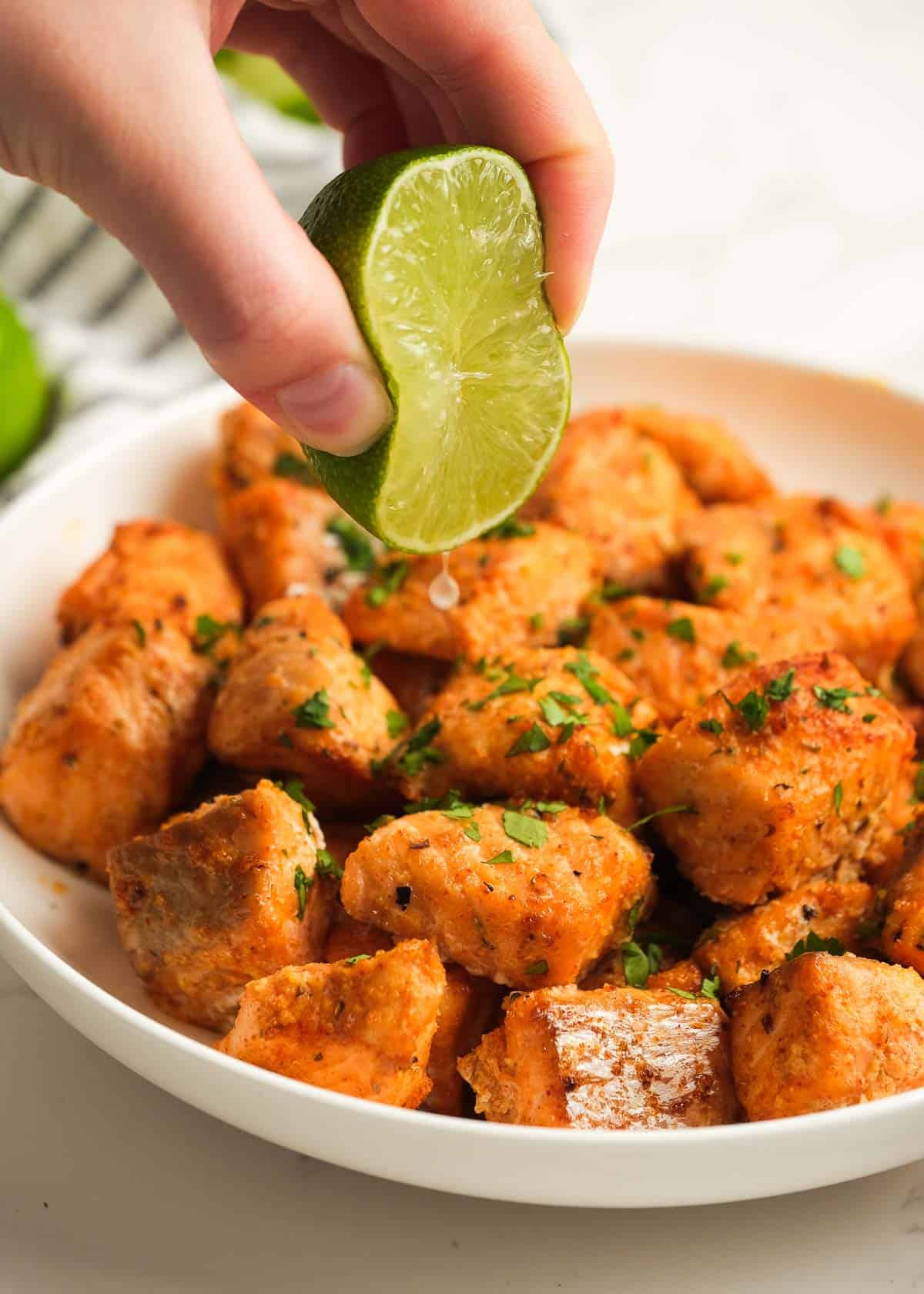 a hand squeezing half a lime over air fryer salmon bites