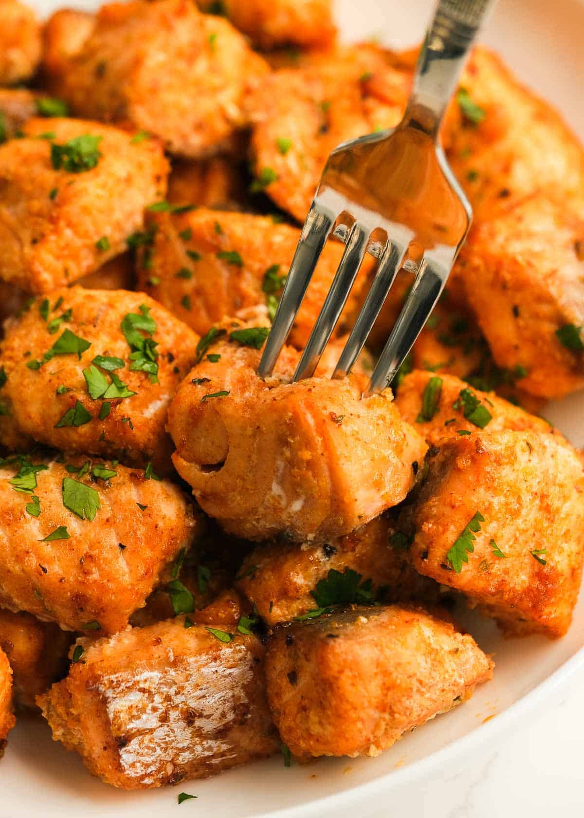 closeup view of salmon bites, fork sticking into one flaky salmon piece