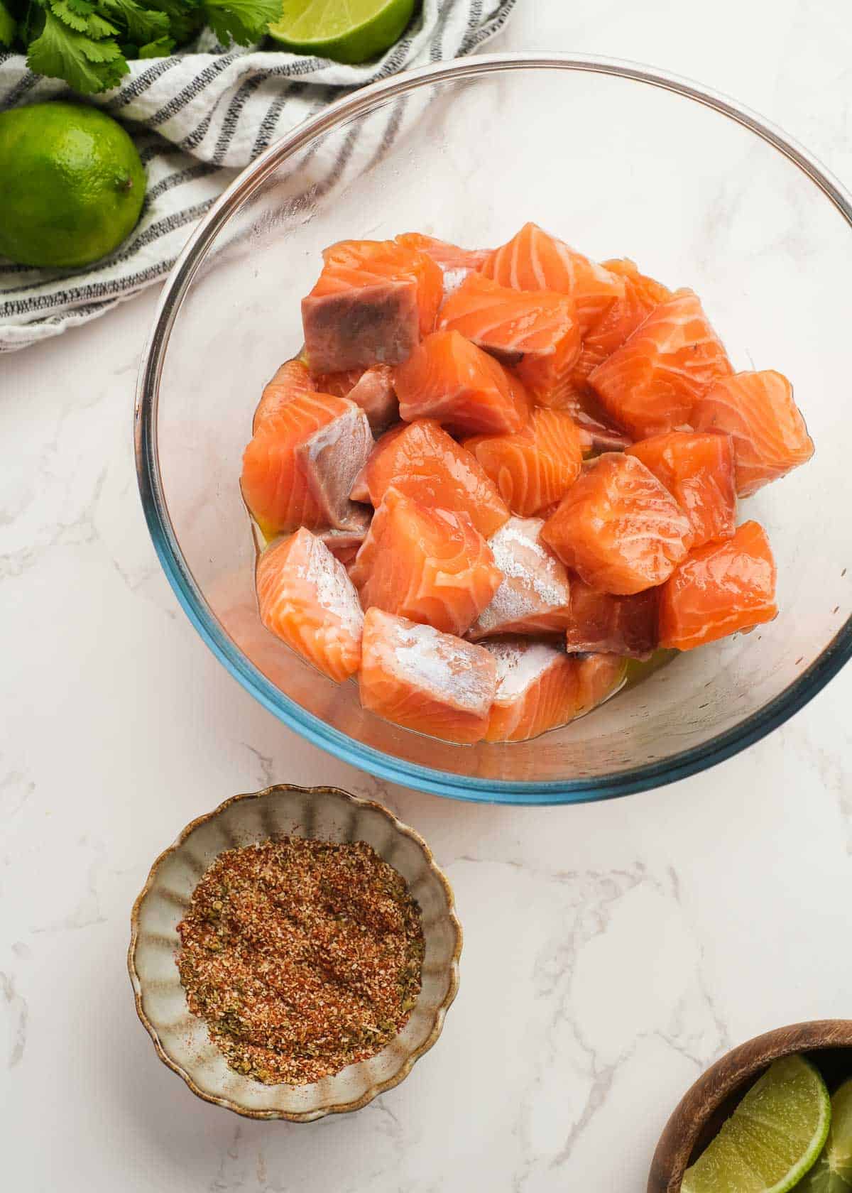 skinless salmon filets cut into cubes in a glass bowl beside a small bowl of seasoning