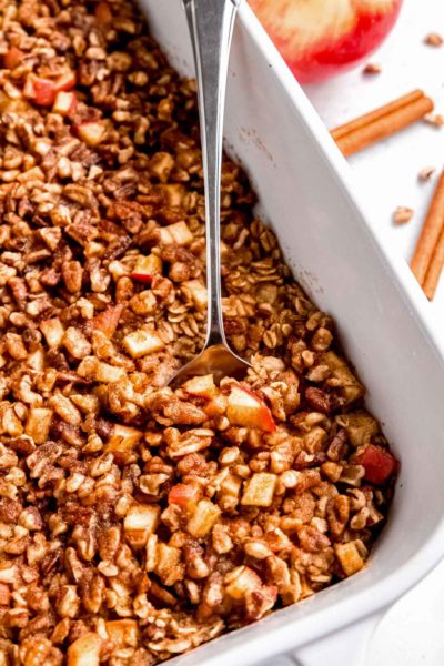 a spoon in cooked apple cinnamon baked oatmeal in a white baking dish