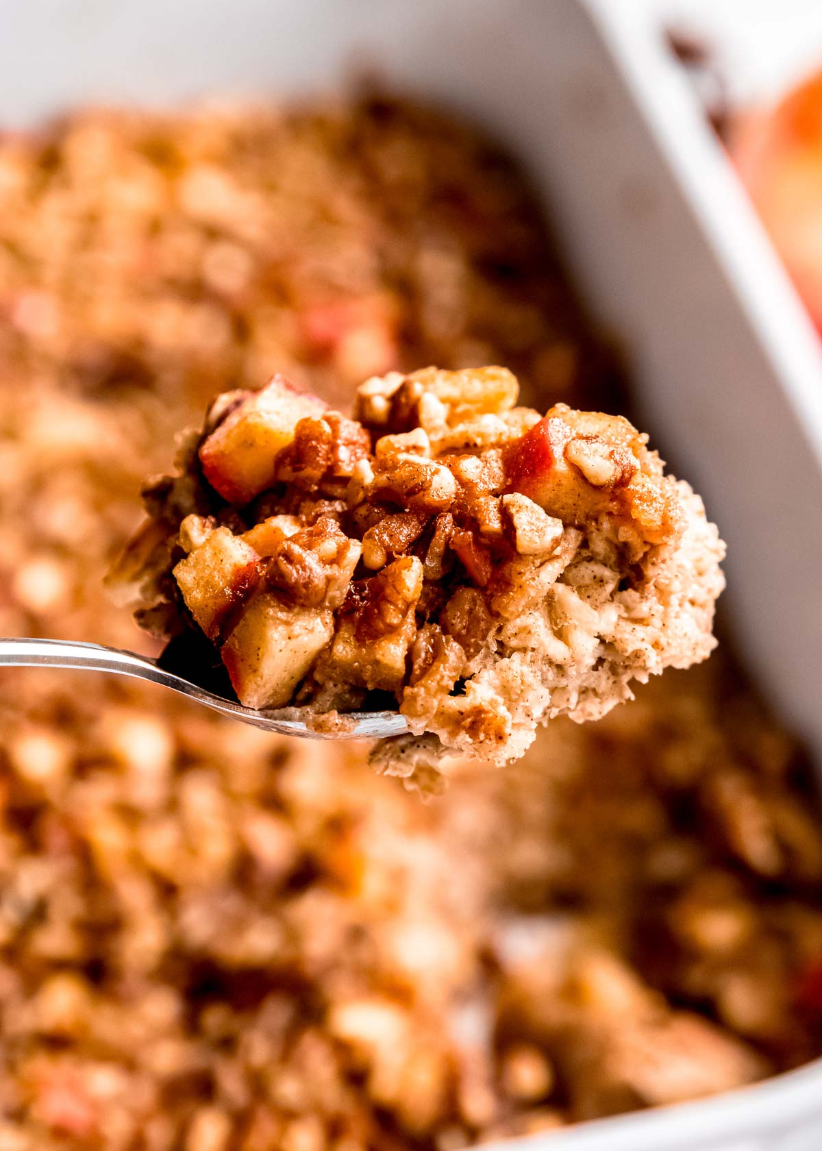a closeup of a large spoon full of baked oatmeal with apples, cinnamon, and pecans