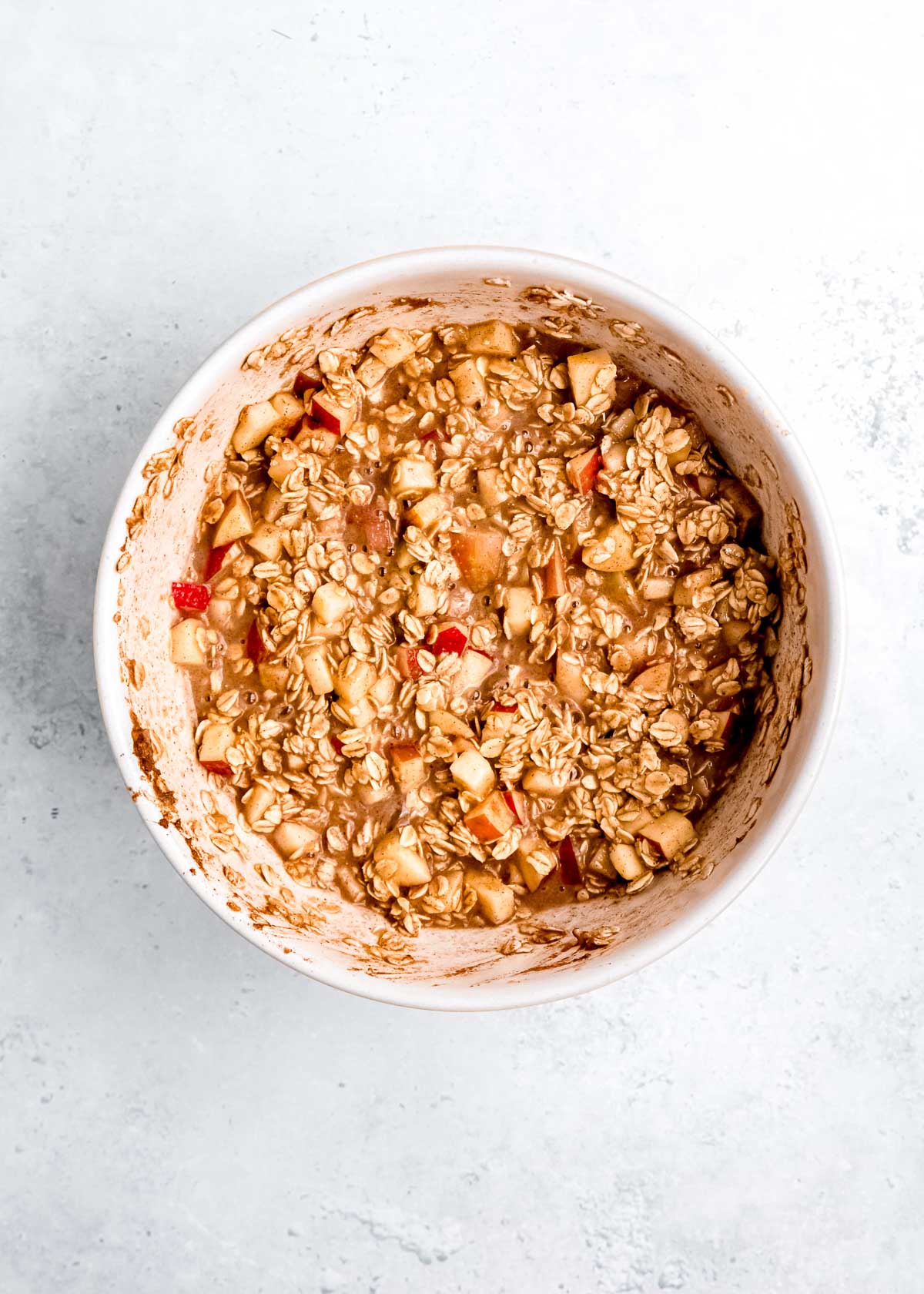 apples, oats, maple syrup, almond milk, apple butter, and other oatmeal ingredients mixed in a white bowl