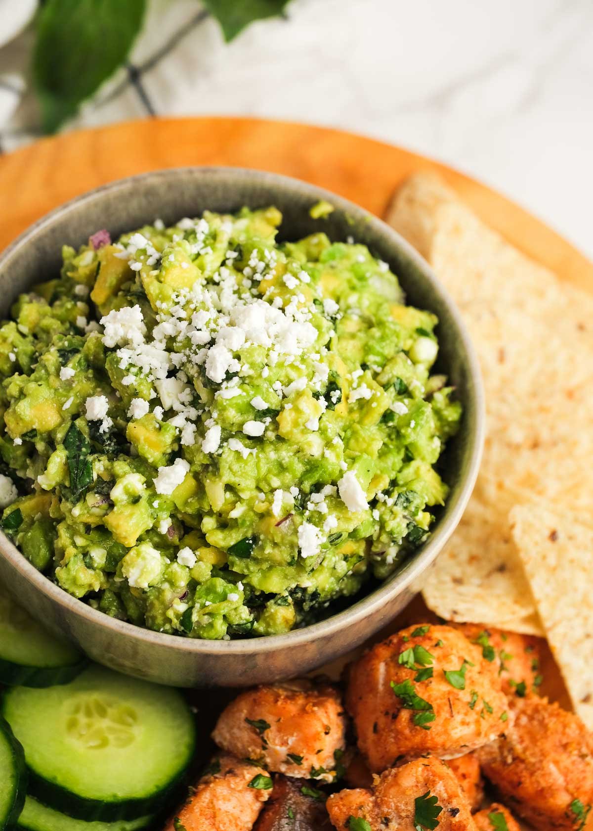 A bowl of avocado feta dip with chips, vegetables and salmon