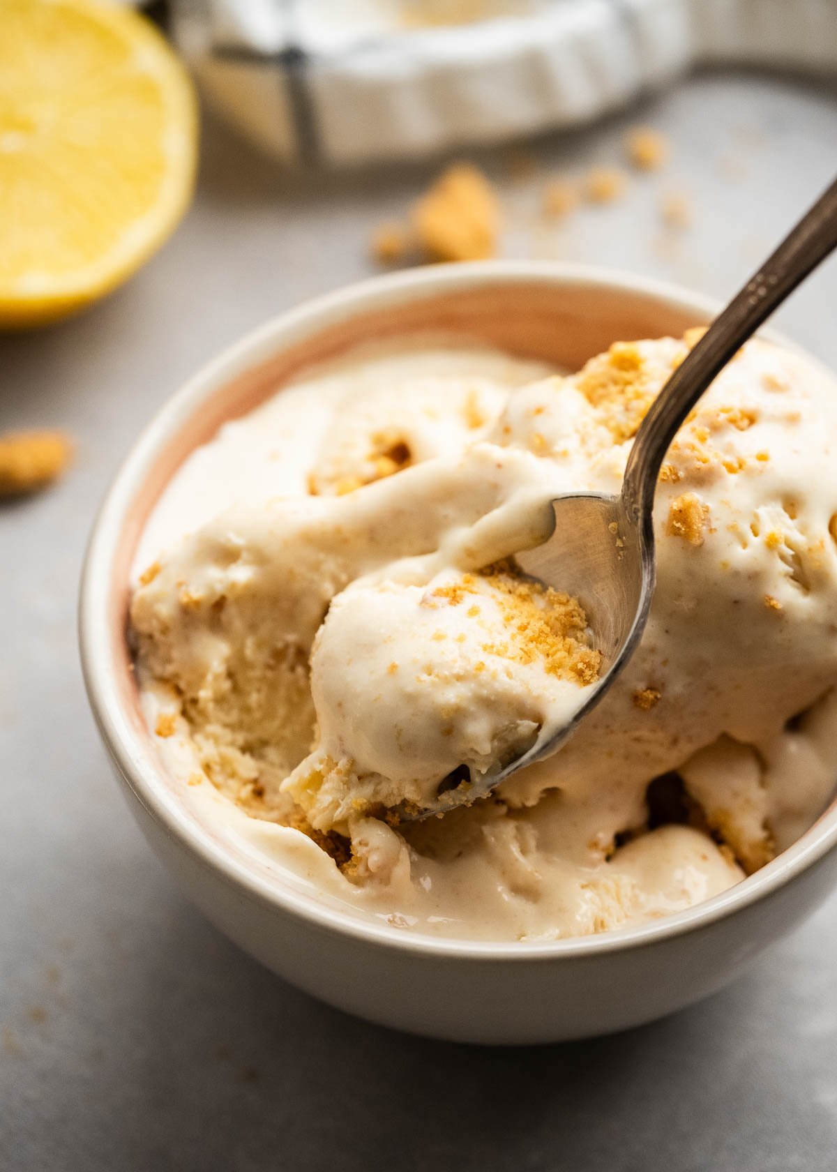 an overhead shot of lemon ice cream in a bowl with a spoon and graham cracker crumbs. 