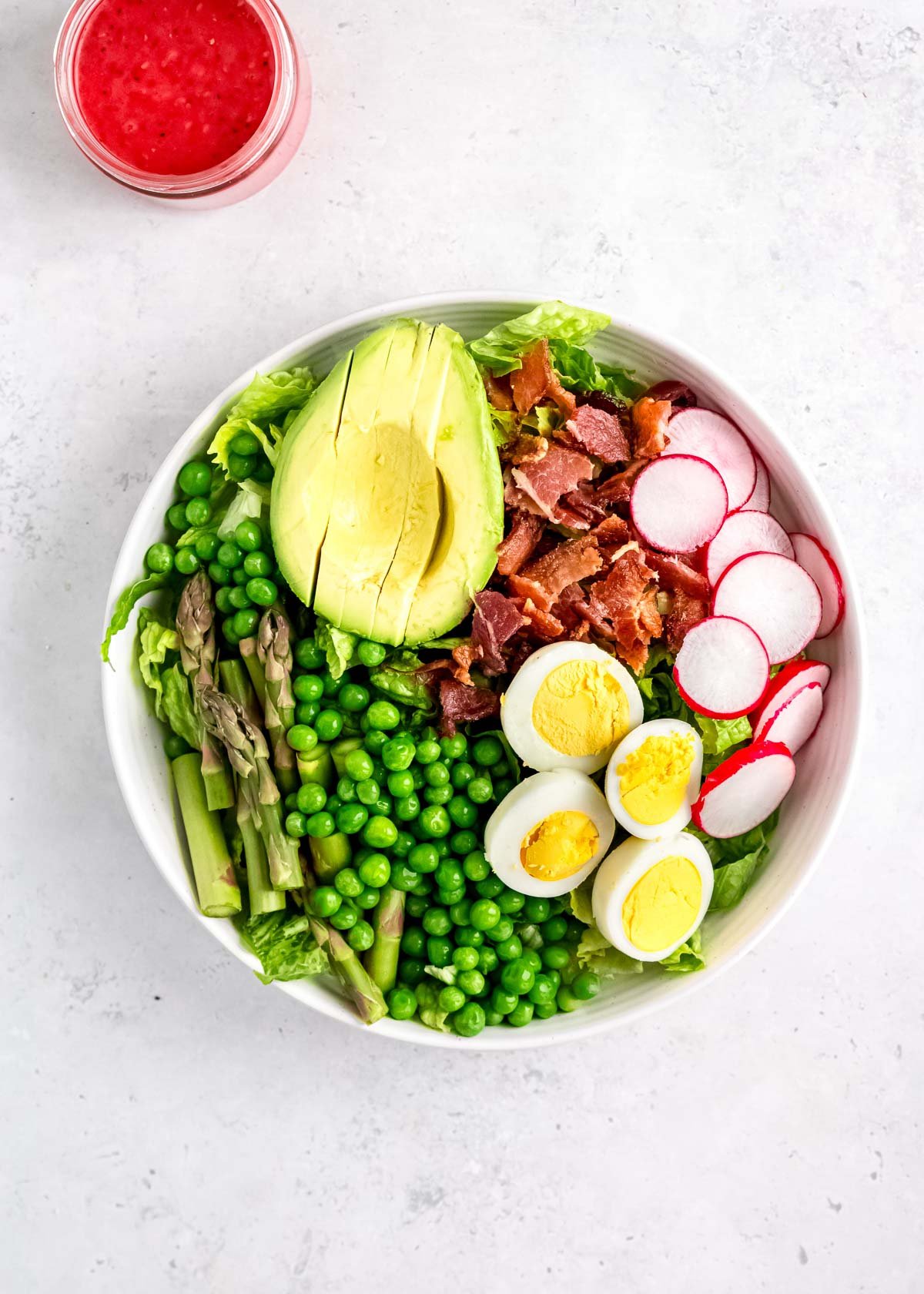 asparagus, avocado, peas, bacon, radishes, eggs, and lettuce in white bowl
