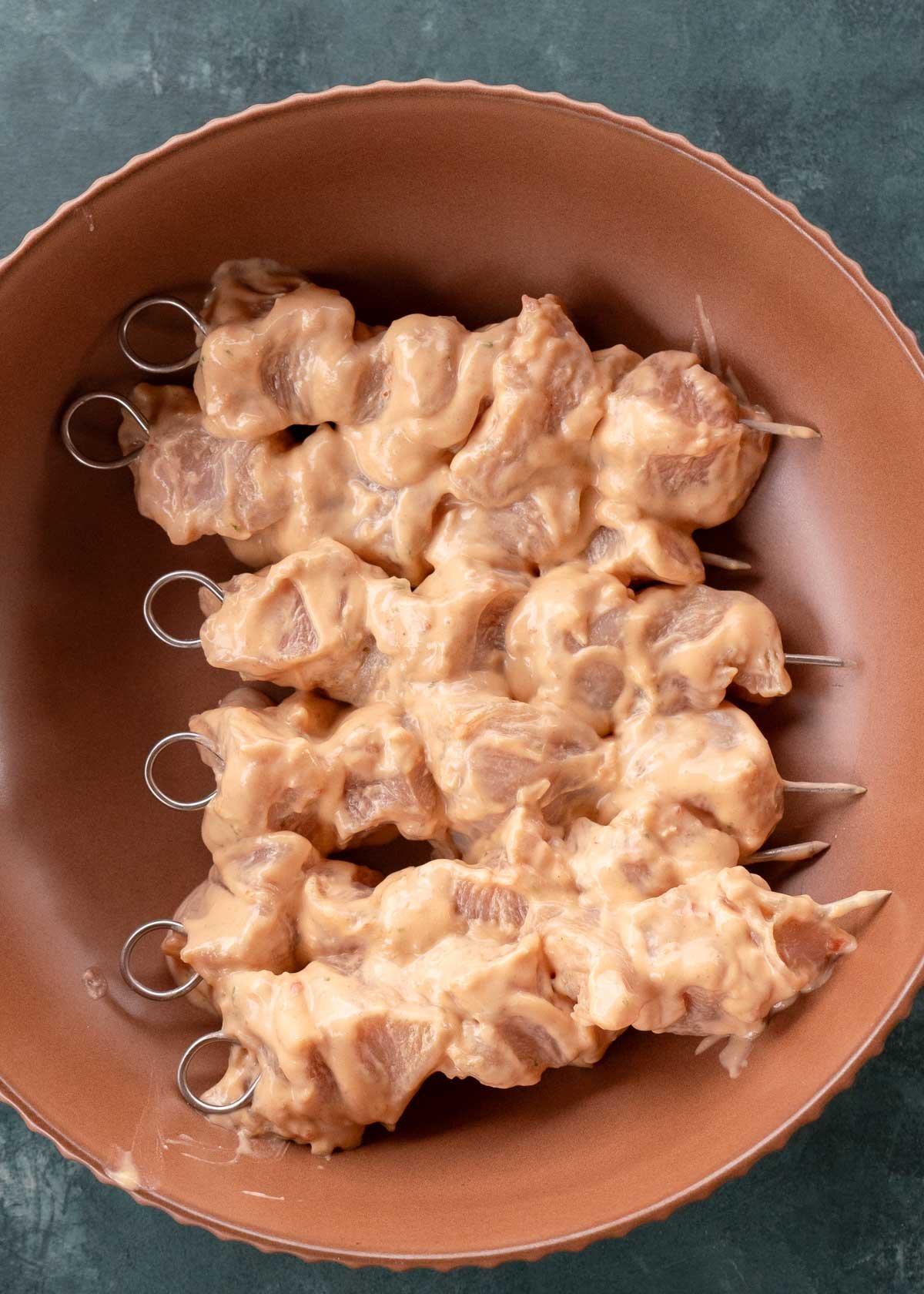 overhead image of raw chicken skewers in brown bowl