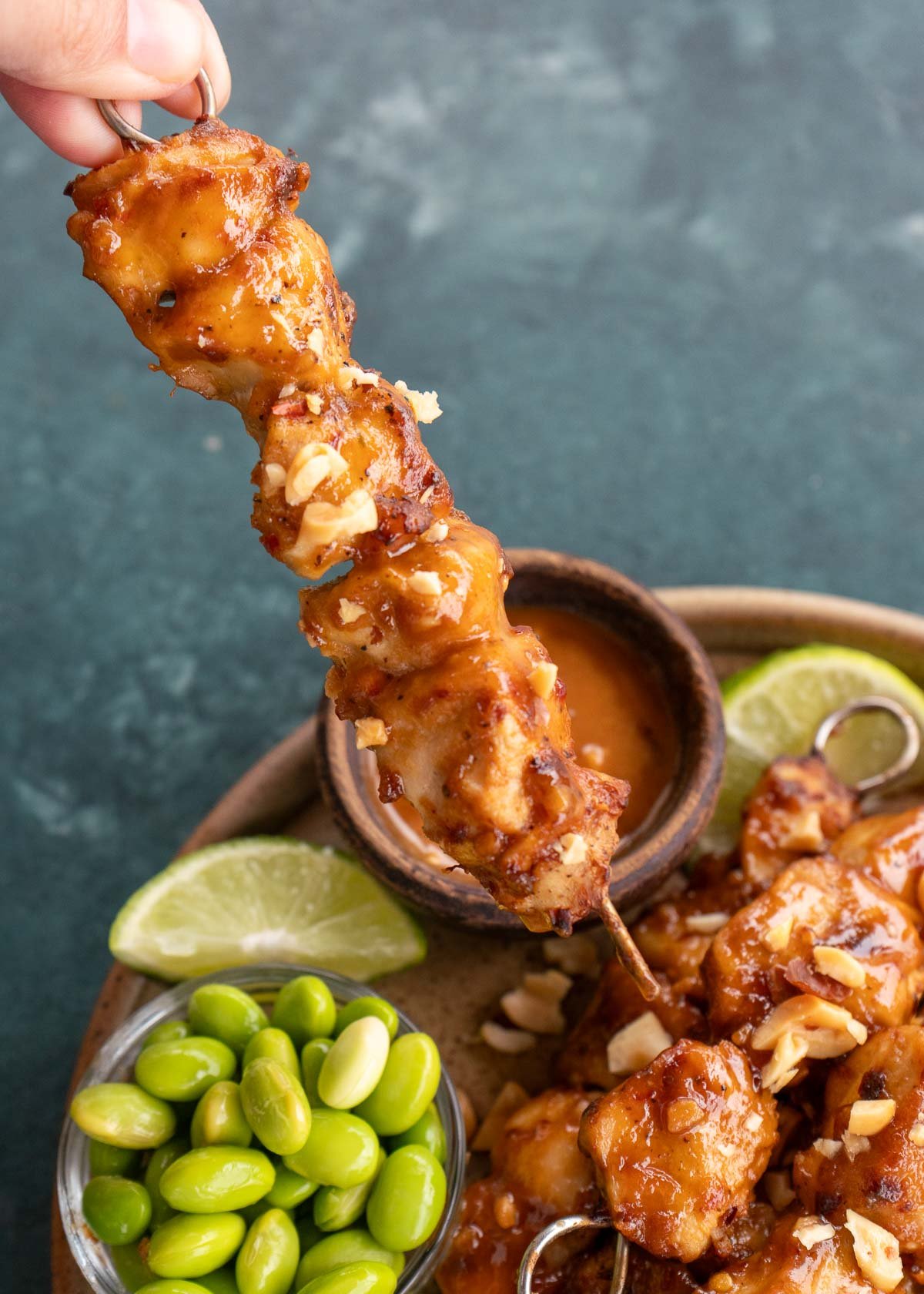 a thai chicken skewer being held over brown plate with additional chicken skewers