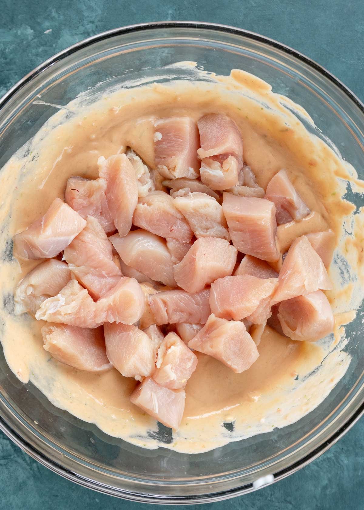 raw chicken being added to bowl with peanut sauce