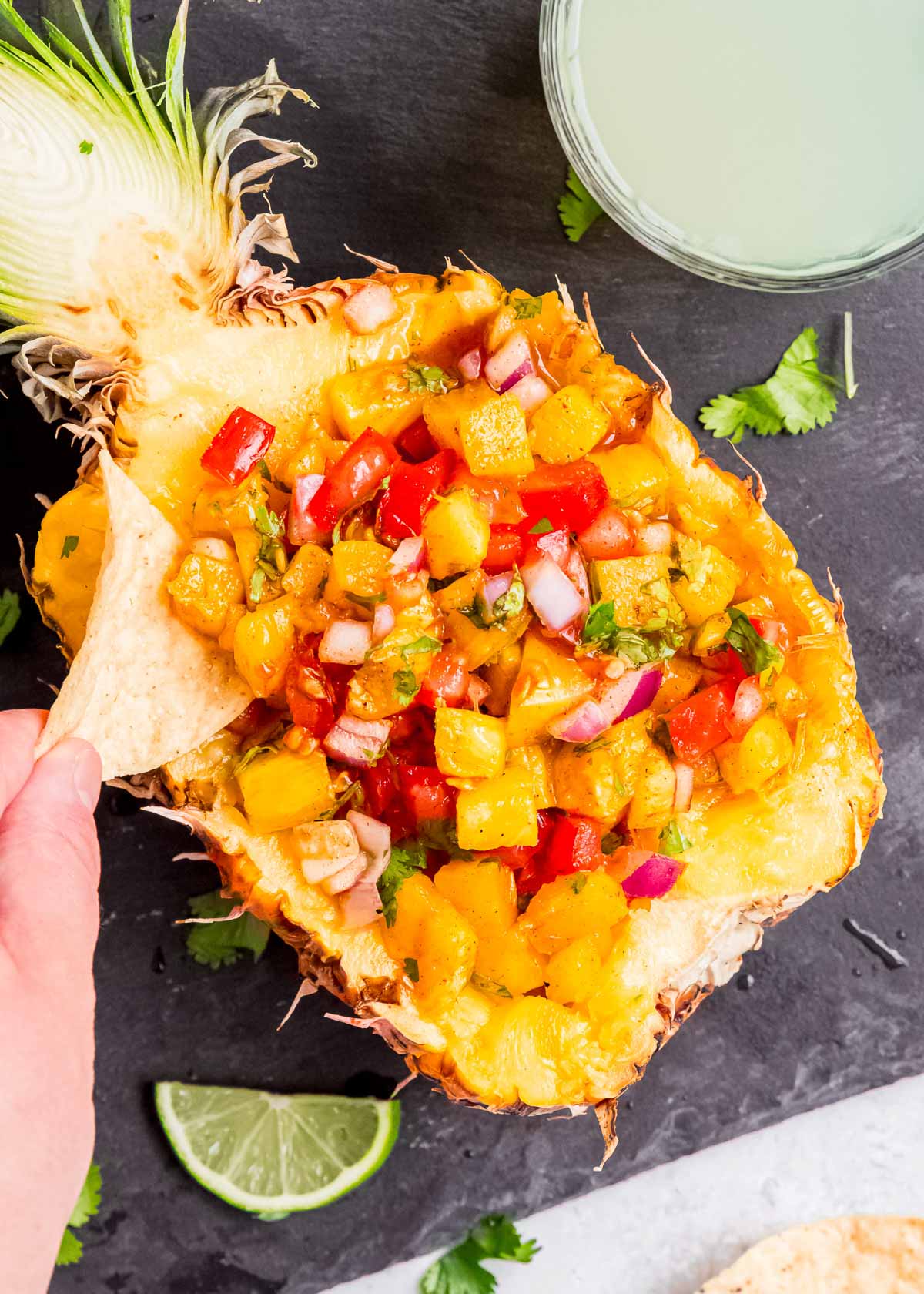 pineapple filled with grilled pineapple salsa; hand dipping a chip into the salsa