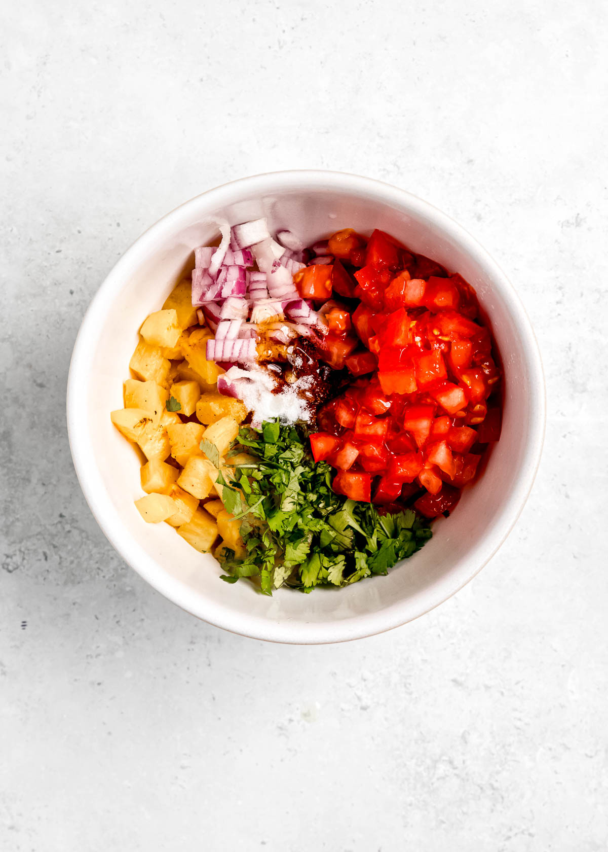 diced pineapple, tomato, red onion, and cilantro in a white bowl