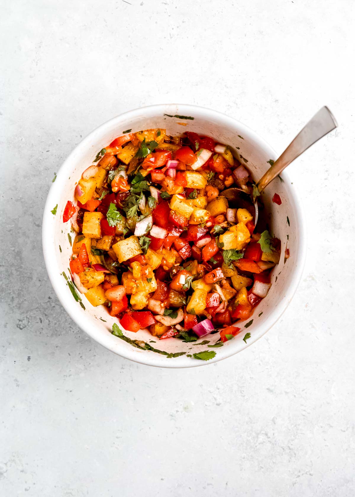 pineapple salsa mixed together in a white bowl with a metal spoon