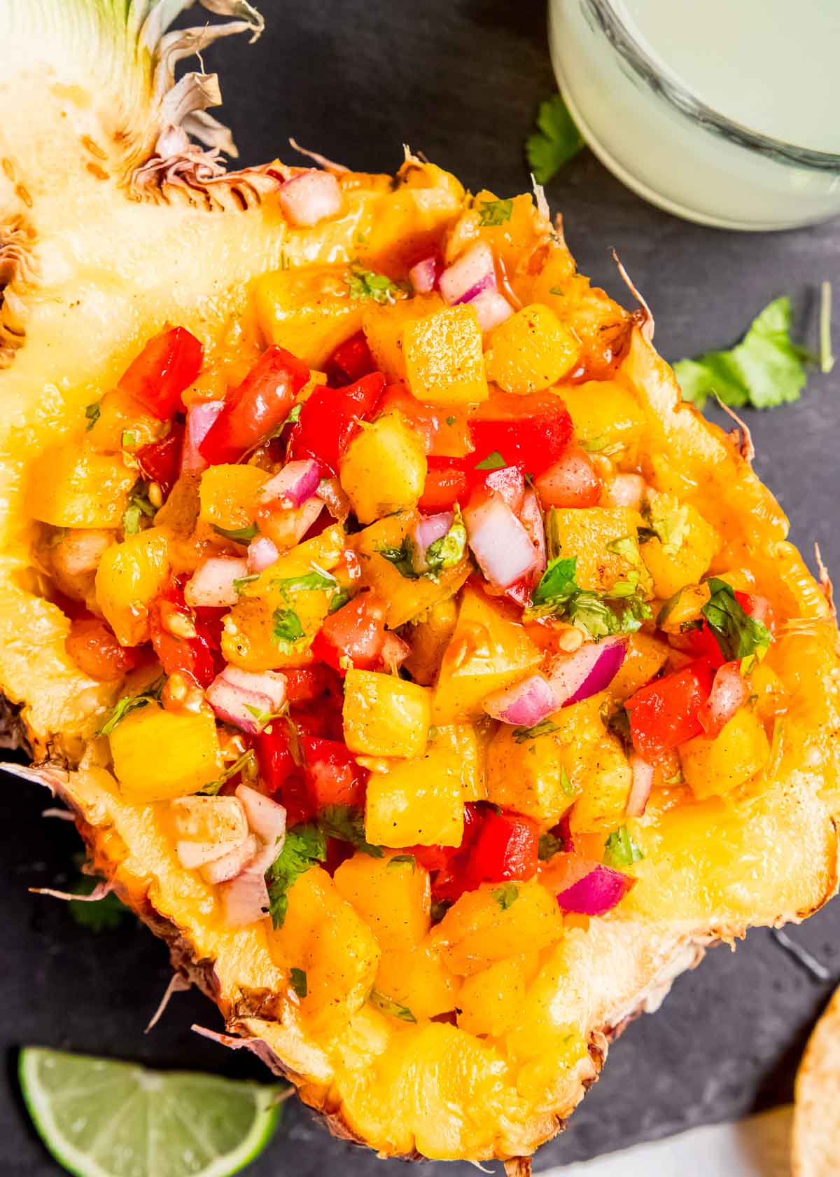 a hollowed-out pineapple filled with delicious grilled pineapple salsa on a black serving board with limes