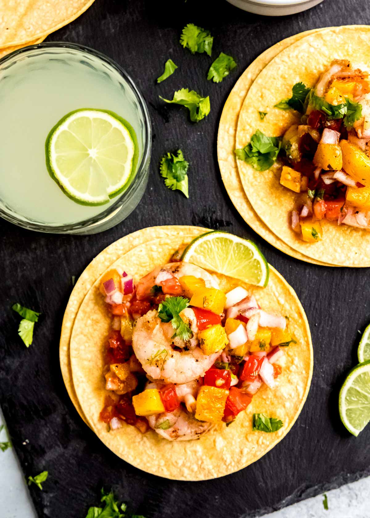 overhead shot of grilled shrimp tacos with a margarita, surrounded by lime wedges and cilantro