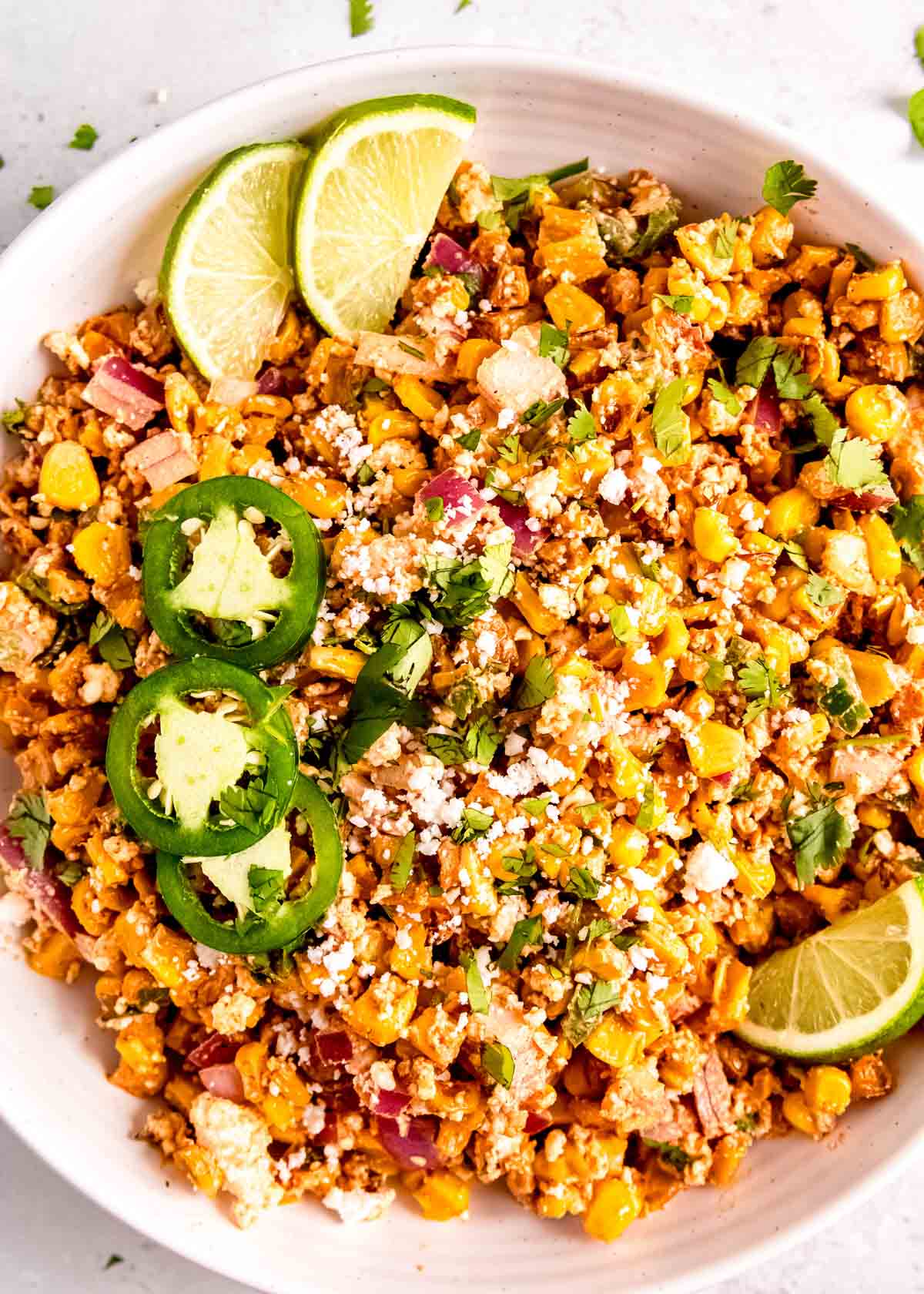 close up image of Mexican street corn in white bowl topped with jalapenos